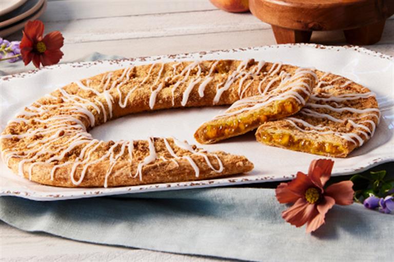 Peach Cobbler Kringle surrounded by flowers on on a white tray. 